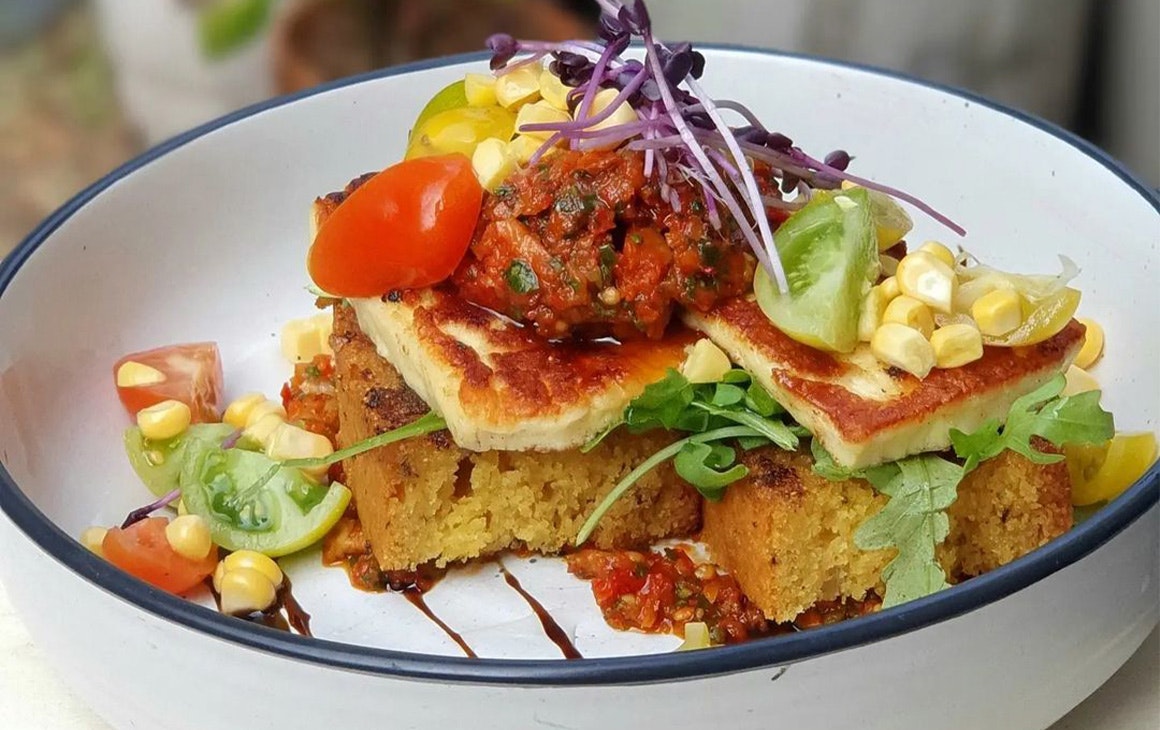 Thick, soft toast with halloumi, relish, tomato, corn and sprouts stacked on.